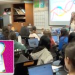 Erin Andrade, professora de pesquisa forense e biotecnologia, sorrindo com alunos visíveis atrás de uma janela.