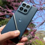 Dois telefones Motorola Razr ao lado de um Samsung Galaxy Z Flip sujo, cercado por coroas douradas flutuantes em um fundo azul claro.