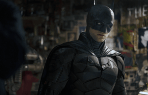 A estrela mais subestimada de ‘The Batman’ retornando oficialmente para ‘The Batman Parte II’ A man in a dark black costume stands in a room covered in photos