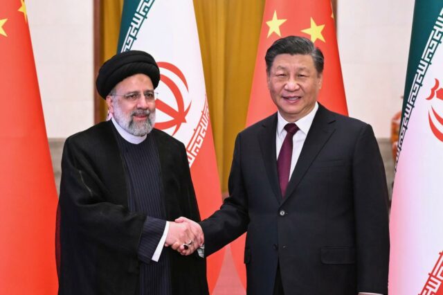 O presidente iraniano, Ebrahim Raisi, e o presidente chinês, Xi Jinping, apertam as mãos diante de suas bandeiras nacionais.
