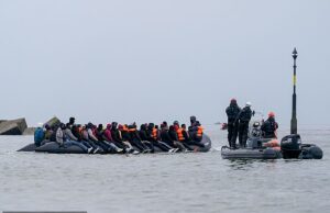 A polícia francesa observa enquanto os migrantes entram no mar para embarcar em barcos com destino ao Reino Unido – dias depois de quatro terem morrido na tentativa de travessia Imagens tiradas na segunda-feira mostraram o bote sobrecarregado flutuando na costa de Dunquerque, com outro seguindo em direção ao Reino Unido, mais à frente.