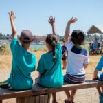 Alunos levantando as mãos para se voluntariarem ou fazerem perguntas ao professor em uma aula sobre natureza ao ar livre.