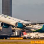 Mark Tighe falando. Ele está do lado de fora e veste um blazer cinza e uma camisa listrada branca e cinza. Ele tem cabelos grisalhos e barba.