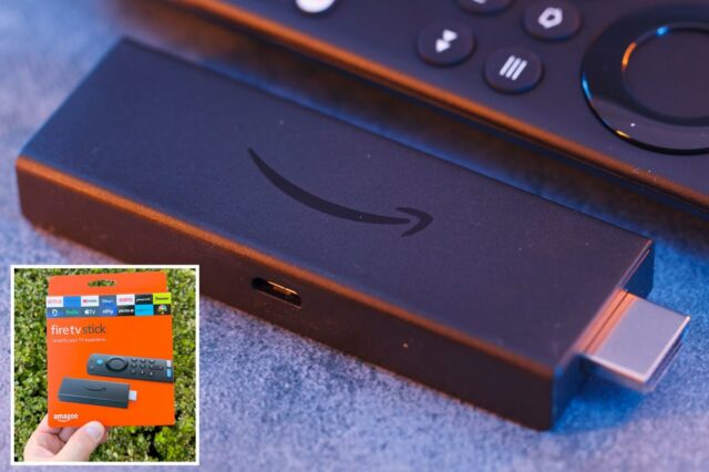 Mão segurando uma embalagem laranja do dispositivo de streaming Amazon Fire TV Stick contra um fundo de folhagem verde.