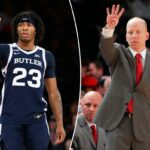 Um jogador de basquete vestindo uma camisa azul escura do Butler com o número 23 aponta o dedo indicador direito para cima.