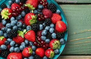 Bomba de fibra de 60 calorias pode aumentar a memória, melhorar o envelhecimento da pele e até combater doenças gengivais Uma mistura de frutas maduras e coloridas em uma tigela turquesa, incluindo mirtilos, morangos, framboesas, amoras e groselhas, sobre um fundo de madeira rústico.