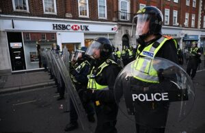 Centenas de manifestantes em Epsom exigem descrição de homens ‘que estupraram mulheres fora da igreja’ enquanto ficam cara a cara com a polícia de choque na rua Polícia de choque com escudos enquanto manifestantes saem às ruas de Epsom após uma denúncia de estupro