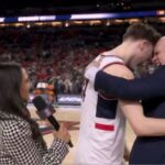Um jogador e um técnico de basquete se abraçam na quadra durante uma entrevista, com um