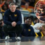 O técnico do Michigan, Dusty May, assiste ao jogo do lado de fora, agachado.