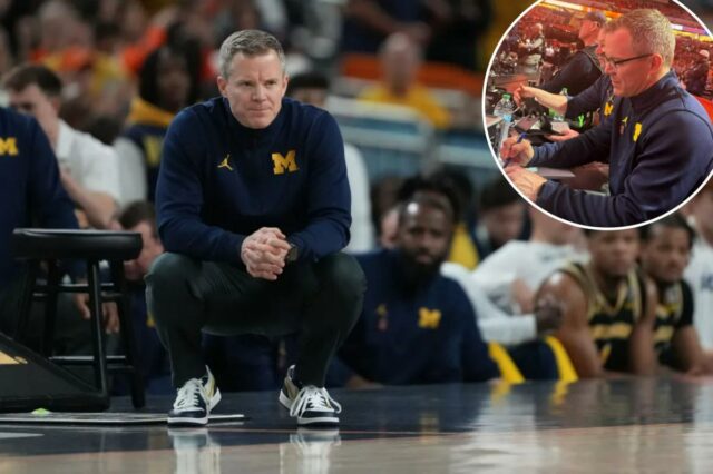 O técnico do Michigan, Dusty May, assiste ao jogo do lado de fora, agachado.