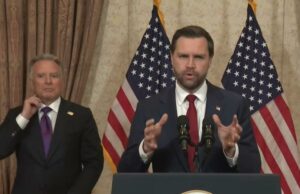 EUA e Irã não conseguem chegar a acordo de paz após maratona de negociações no Paquistão JD Vance falando em um pódio com duas bandeiras americanas atrás dele.