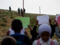 Enquanto o arame farpado bloqueia as crianças nas aulas, os palestinos encenam a ‘Escola da Liberdade’ Khalil e Tareq seguram faixa com crianças (Jacob Lazarus/Al Jazeera)