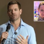 Angela Belcamino, de longos cabelos loiros, vestindo camisa prateada de botões e brincos de cobra, sorri para a câmera com caça-níqueis visíveis ao fundo.