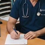 As pessoas sentam-se na sala de espera do médico. Uma mulher olha um folheto médico e um homem usa seu smartphone para fazer uma ligação.