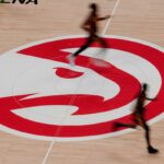 Jogadores de basquete passam correndo pelo logotipo do Atlanta Hawks na quadra.