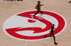 Ex-executivo do Hawks que desviou mais de US$ 3,7 milhões da equipe foi condenado a mais de 3 anos de prisão Jogadores de basquete passam correndo pelo logotipo do Atlanta Hawks na quadra.