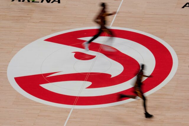 Jogadores de basquete passam correndo pelo logotipo do Atlanta Hawks na quadra.