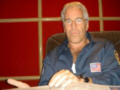 Fiscalizador do Departamento de Justiça que analisa a conformidade com a lei determina a divulgação dos arquivos de Epstein Jeffrey Epstein em uma camisa azul escura com um emblema da bandeira americana, sentado em uma cadeira.