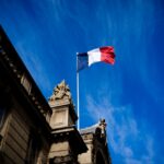 French tricolour flag (blue, white and red, symbol of the Republic of France) hanging from a flagpole above the entrance gate to the courtyard of the Elysee Palace, Exit from the Cabinet meeting at the Presidential Palace of the Elysee in Paris, France on August 27, 2025. The ministers get into their cars and leave the Elysee Palace. (Photo by Amaury Cornu / Hans Lucas via AFP)