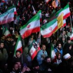 Uma grande multidão de pessoas segurando bandeiras iranianas à noite.