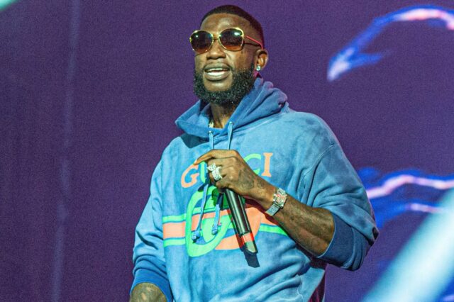 Gucci Mane se apresentando com um moletom Gucci azul e óculos escuros.
