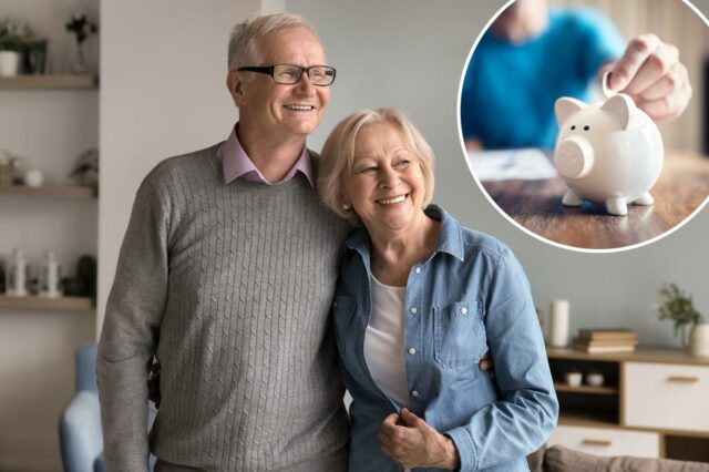 Há um novo ‘número mágico’ para as poupanças viverem ‘confortavelmente’ A mão de uma pessoa inserindo uma moeda em um cofrinho branco sobre uma mesa de madeira.