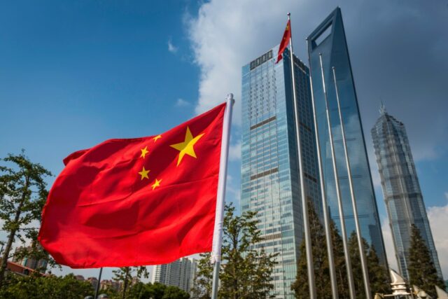 The vibrant red field and yellow stars of the Flag of the People's Republic of China flying in the breeze beside the futuristic glass and steel towers of Pudong's soaring skyscrapers, Shanghai, China.