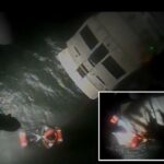 Um nadador de resgate da Guarda Costeira é içado da água com uma pessoa resgatada de um iate a motor desativado à noite.