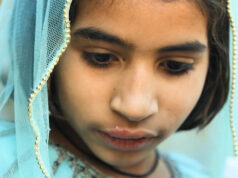 Hospital no centro do surto de HIV infantil é pego reutilizando seringas em filmagem secreta Um homem sentado em uma cadeira usando um estetoscópio, máscara facial e luvas cumprimenta uma mulher segurando seu filho. Os rostos da mulher e da criança estão obscurecidos.