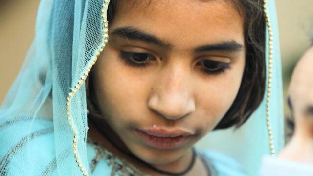 Hospital no centro do surto de HIV infantil é pego Um homem sentado em uma cadeira usando um estetoscópio, máscara facial e luvas cumprimenta uma mulher segurando seu filho. Os rostos da mulher e da criança estão obscurecidos.