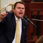 O deputado Ken Calvert fala em uma coletiva de imprensa anunciando apoio a uma medida de identificação do eleitor, cercado por pessoas segurando cartazes que dizem