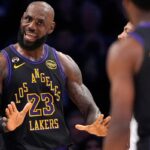 LeBron James com uniforme do Lakers com as mãos para cima, de frente para Bronny James, que está de costas para a câmera.