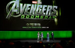 Marvel Studios retornará ao Hall H da Comic-Con neste verão | Exclusivo Robert Downey Jr. está no palco da Comic-Con fantasiado de Victor Doom e segura sua máscara voltada para o céu em um gesto triunfante