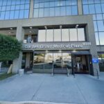 Exterior do Garden Grove Medical Plaza com uma árvore, bancos e estacionamento visíveis.