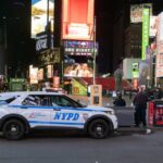 Um carro da polícia de Nova York estacionado à noite na Times Square, na cidade de Nova York, cercado por grandes outdoors e anúncios bem iluminados.