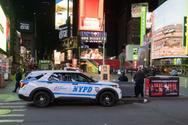 Um carro da polícia de Nova York estacionado à noite na Times Square, na cidade de Nova York, cercado por grandes outdoors e anúncios bem iluminados.
