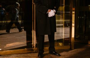 Milhares de porteiros e supers de Nova York ‘paralisam’ o estilo de vida chique da cidade com voto de greve Um porteiro de casaco preto e luvas brancas está do lado de fora da Trump Tower.