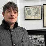 Uma parede de exposição mostrando pinturas e gravuras emolduradas representando Coventry, bem como sinalização antiga.