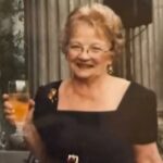 Peggy Fields sorrindo e segurando um copo.