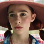 A woman with red hair and a red, wide-brimmed hat