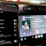 Um SUV prateado em frente ao logotipo do Android Auto em um fundo geométrico verde e azul