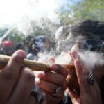 Um homem de óculos escuros exala fumaça de um baseado de maconha em uma celebração de cannabis.