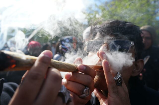 Um homem de óculos escuros exala fumaça de um baseado de maconha em uma celebração de cannabis.