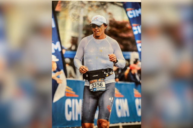 Um homem de terno e gravata borboleta fica em frente a uma parede com o 