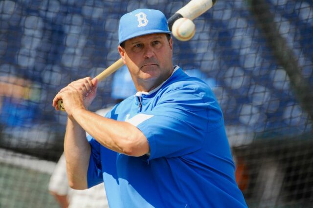 Um jogador de beisebol com boné e camisa azuis segura um taco com uma bola de beisebol acima do ombro.