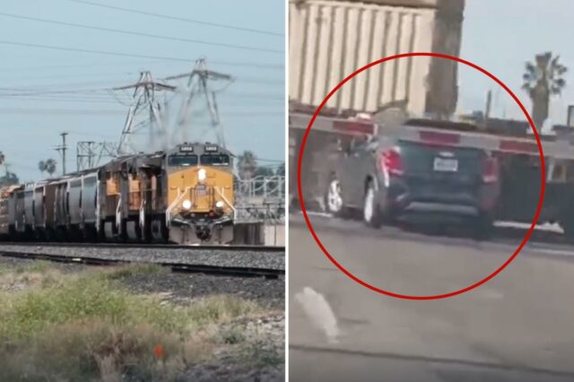 Um SUV de cor escura está preso nos trilhos de uma ferrovia enquanto um trem se aproxima, seu pára-choque traseiro batendo na lateral de um vagão de carga.