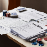 O consultor insta o Reino Unido a interromper as verificações de risco de jogo até que os dados do piloto sejam publicados. O risco financeiro do jogo no Reino Unido verifica a papelada com fichas de cassino na mesa, ilustrando o debate político sobre verificações de acessibilidade