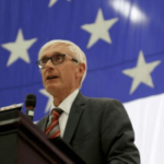 Governador de Wisconsin, Evers, falando no pódio com a bandeira americana ao fundo, abordando a legislação tribal de apostas esportivas móveis