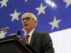 O governador Evers assina projeto de lei que expande as apostas esportivas móveis tribais em Wisconsin Governador de Wisconsin, Evers, falando no pódio com a bandeira americana ao fundo, abordando a legislação tribal de apostas esportivas móveis