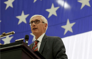 O governador Evers proíbe os funcionários de Wisconsin de explorar informações privilegiadas por meio de mercados de previsão Governador de Wisconsin, Evers, falando no pódio com a bandeira americana ao fundo, abordando a legislação tribal de apostas esportivas móveis